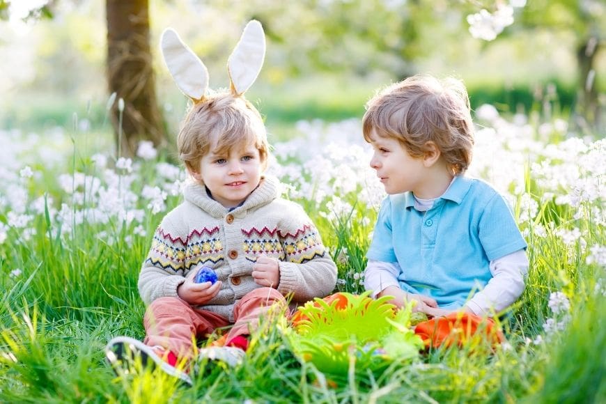 Two small boys, one with bunny ears sat in the grass with their easter eggs 