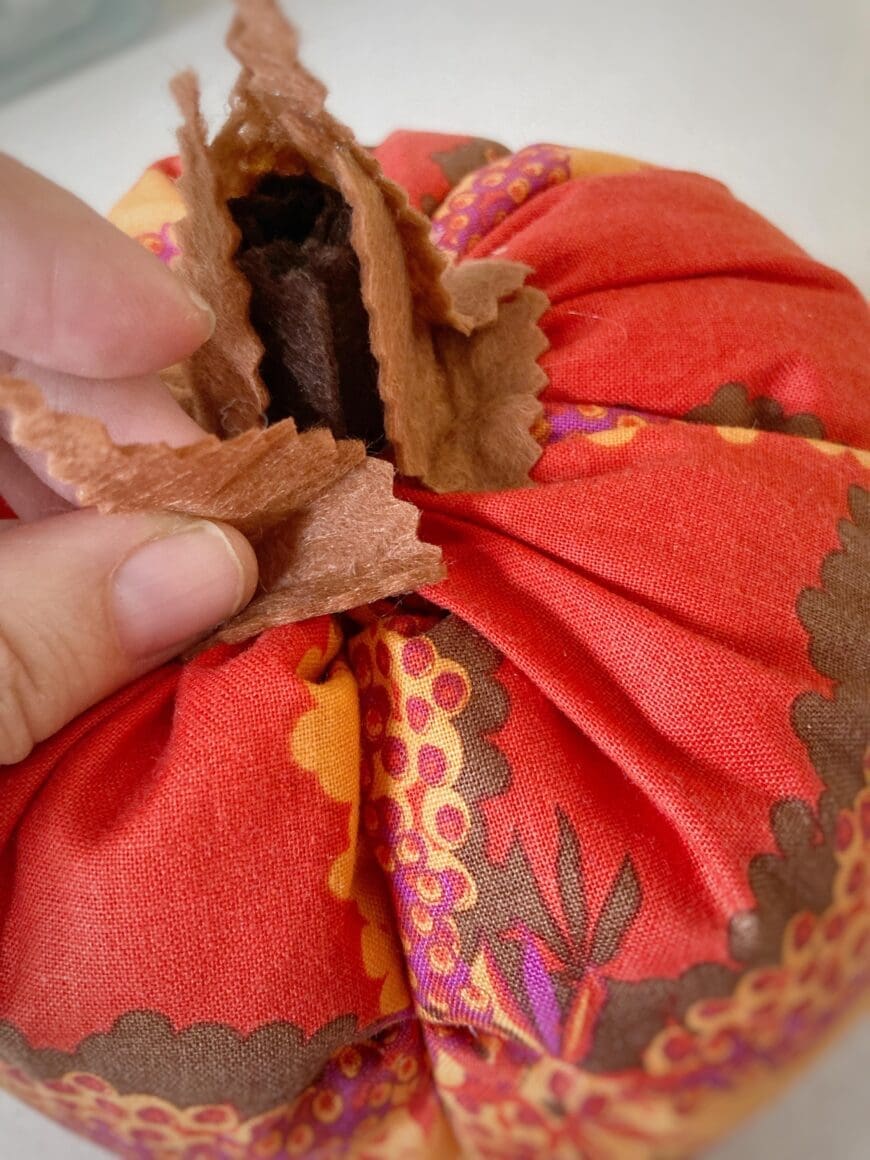 A Red fabric pumpkin with brown felt stalk being added