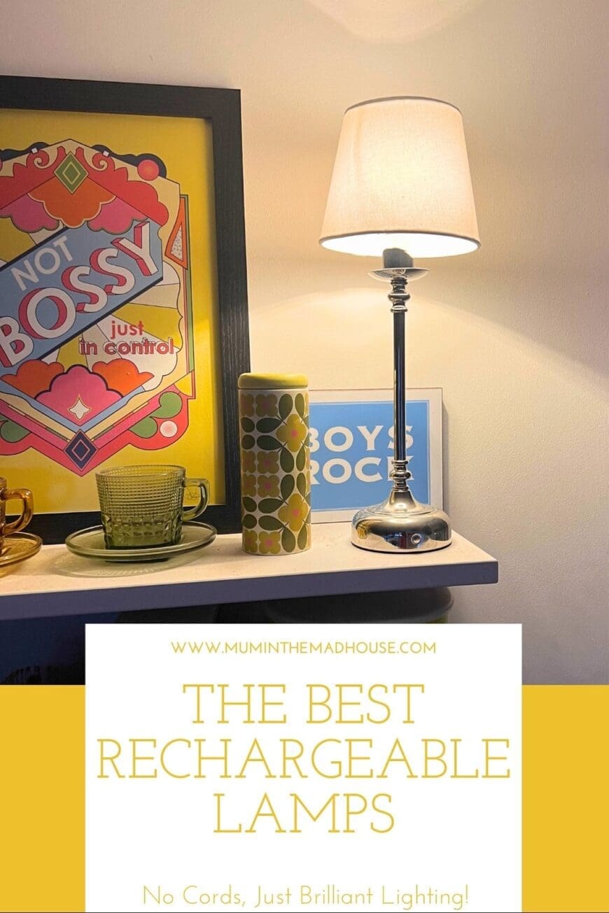 A stylish chrome rechargeable lamp with a white fabric shade placed on a shelf, casting a warm glow. Surrounding decor includes a retro ‘Not Bossy, Just in Control’ framed print, a green glass cup and saucer, and a vintage-inspired ceramic container. A perfect example of cord-free lighting enhancing a cozy home setting.